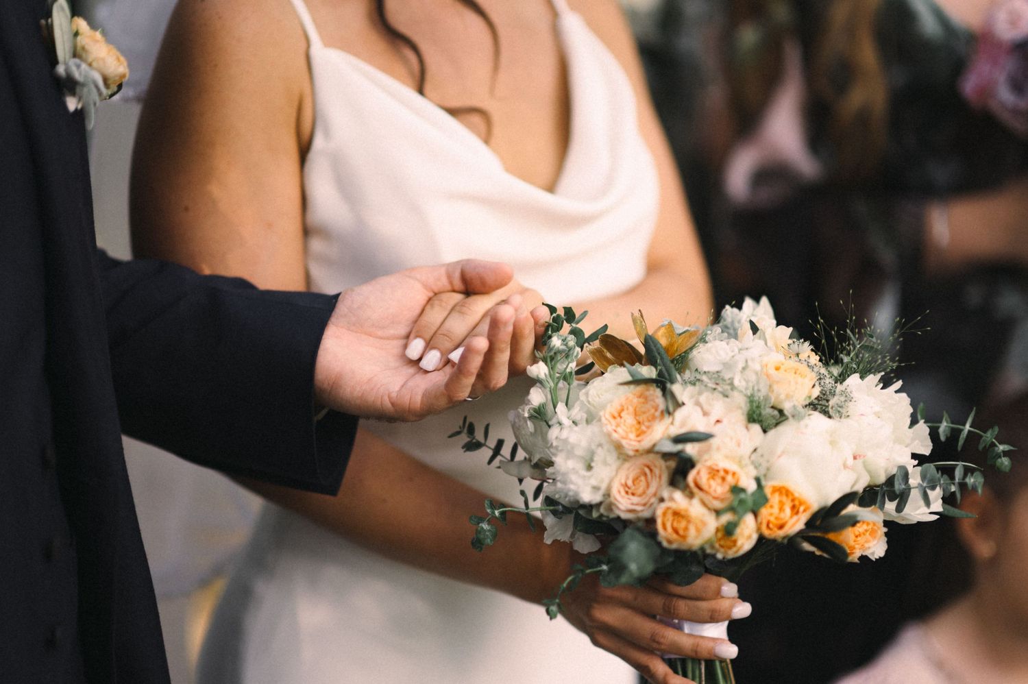Close-up of bouquet and hands during wedding ceremony moment.