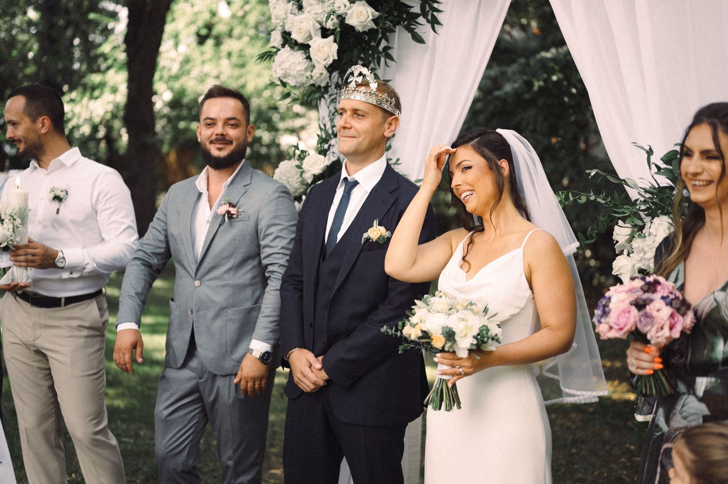 Wedding party gathered under pink draped arch during outdoor ceremony celebrations.