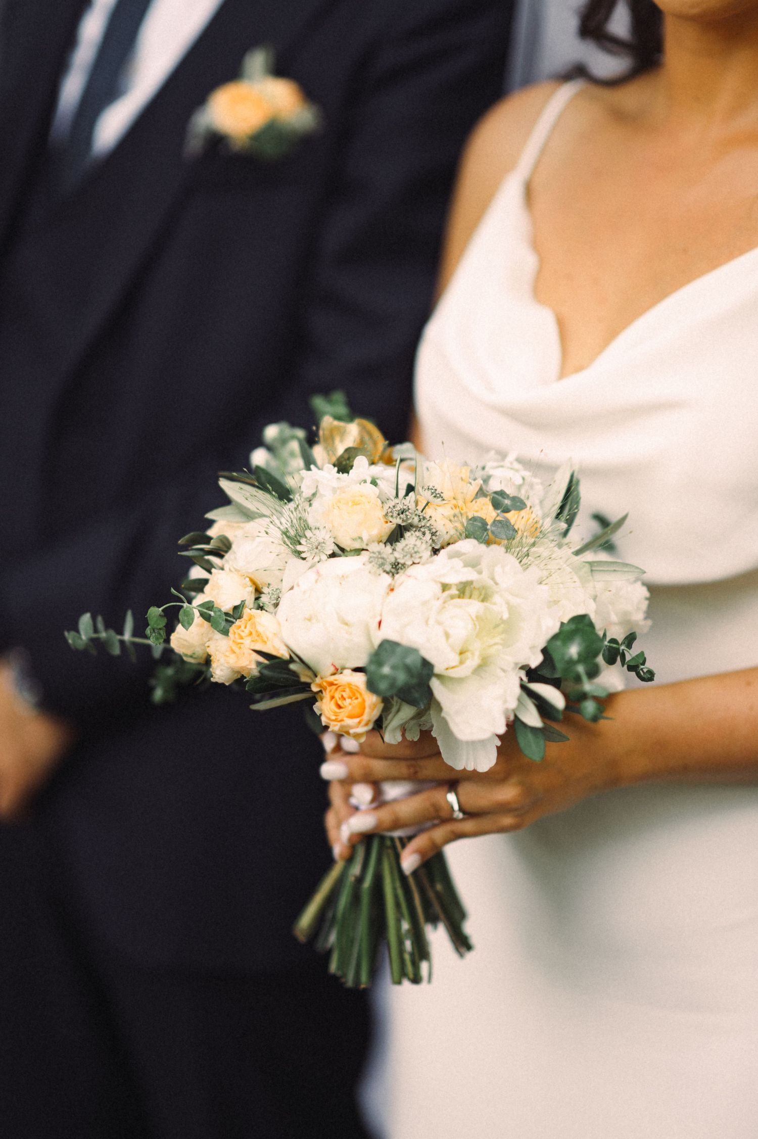 Close-up of bridal bouquet featuring white and peach flowers with greenery against formal attire.
