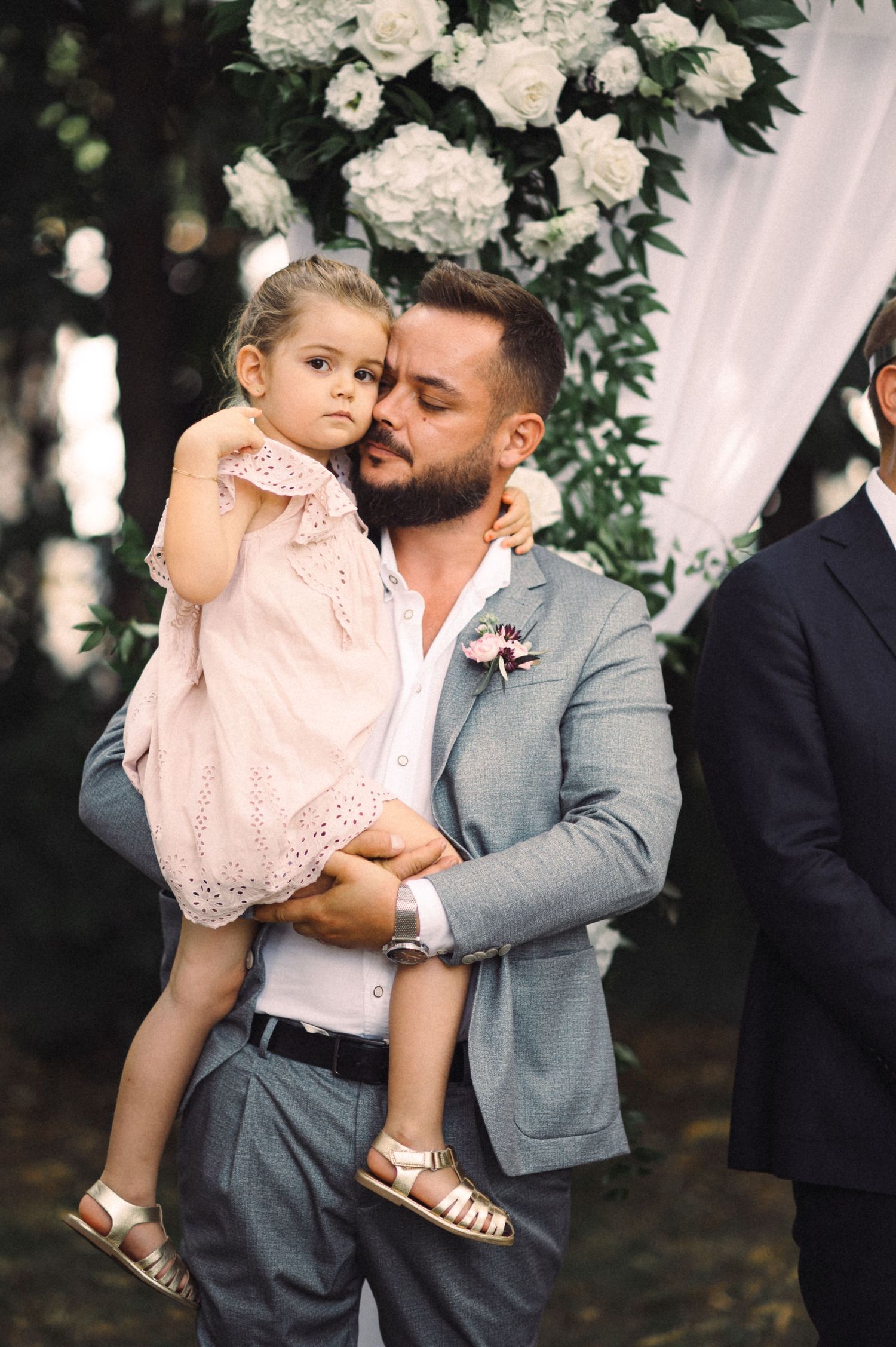 A tender embrace at an outdoor wedding ceremony decorated with white roses and flowing fabric.