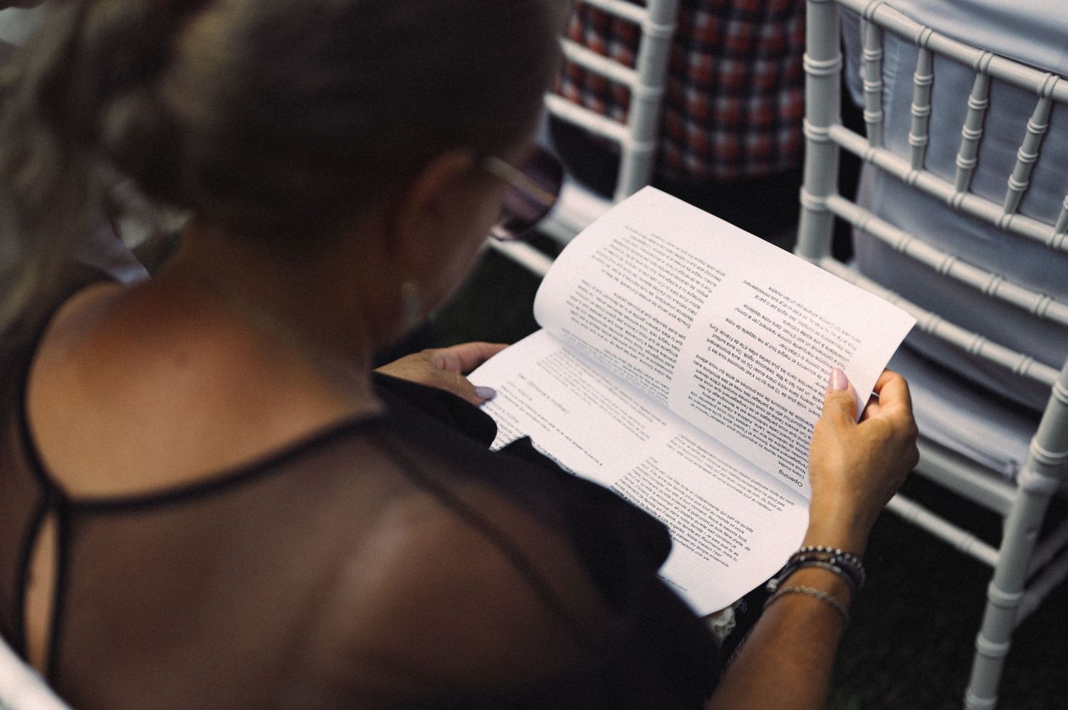 A guest reads from a book while seated in a white chiavari chair.