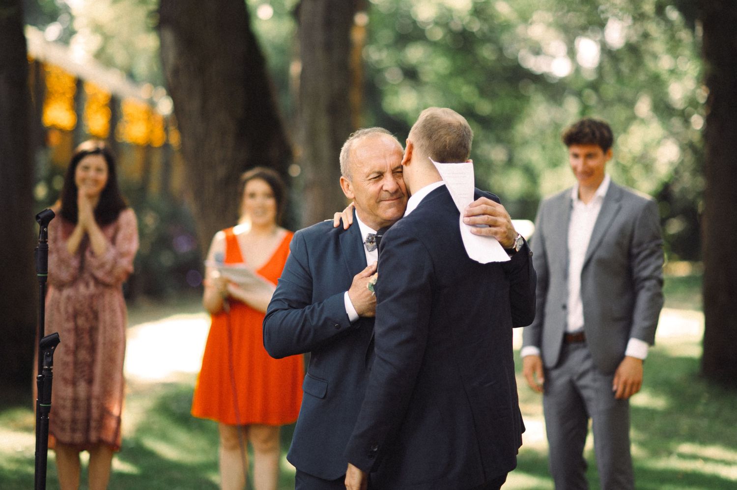 Emotional moment during outdoor ceremony with guests watching in background.