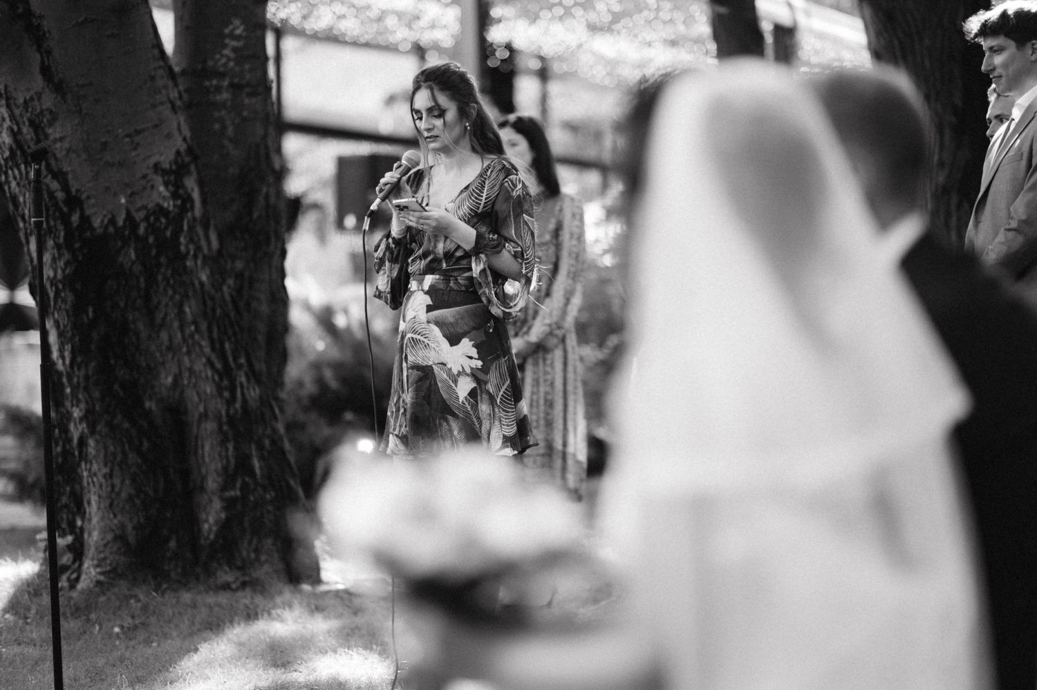 Black and white photo capturing emotional speech during outdoor wedding ceremony.