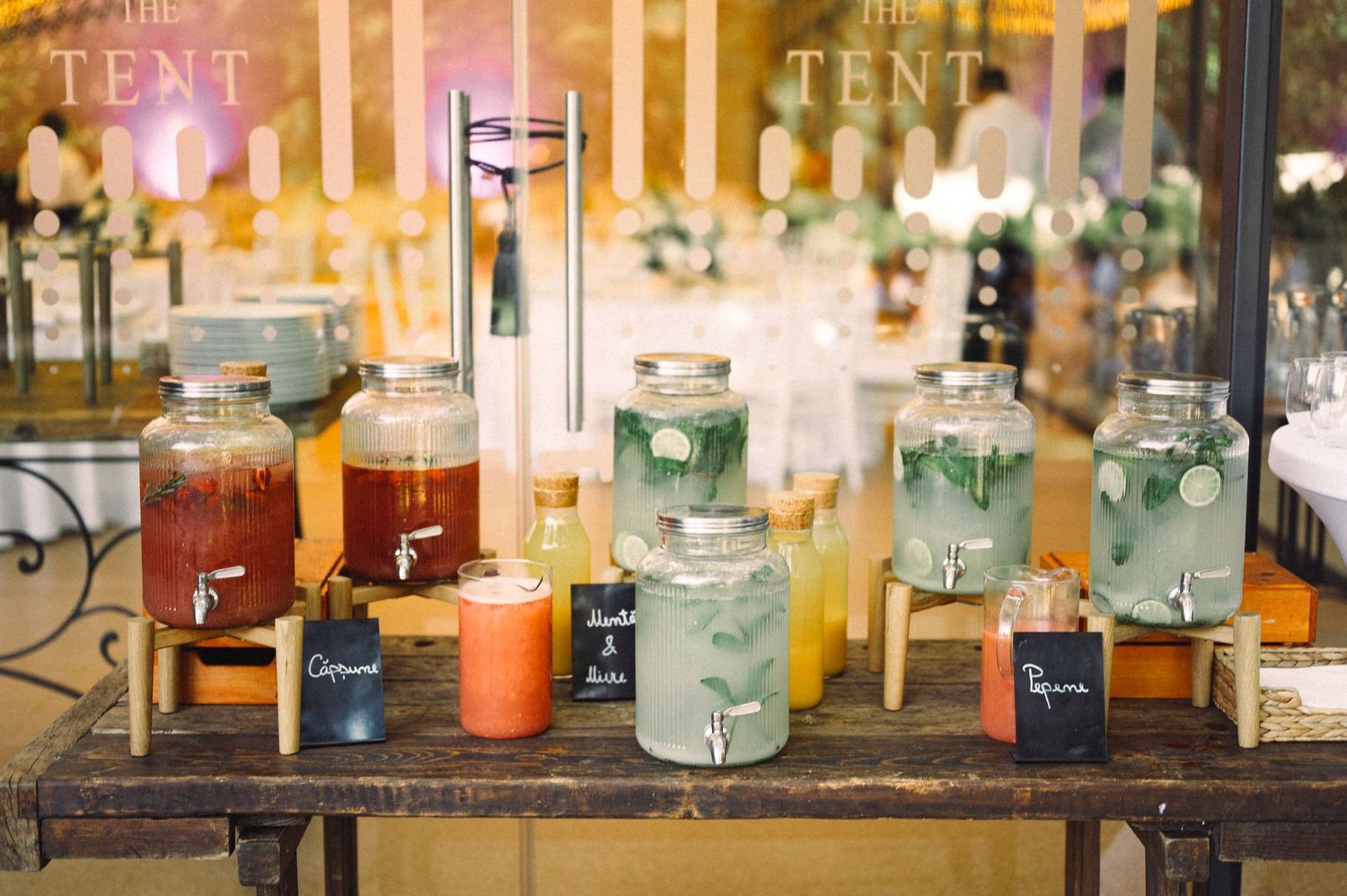 Colorful drink dispensers with various beverages displayed at rustic wedding reception bar.