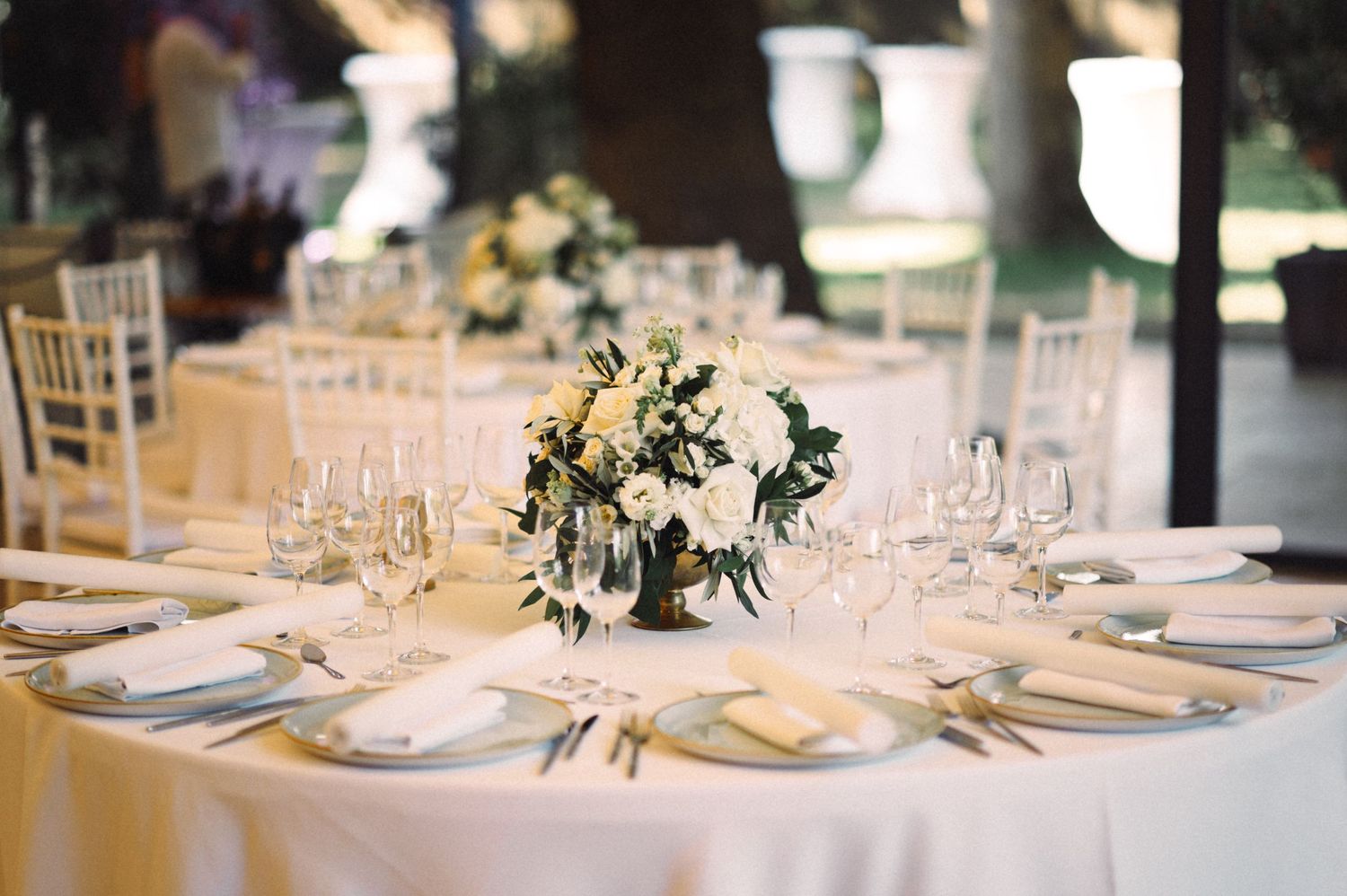 Elegant wedding reception table setting with white linens, crystal glasses and a centerpiece of white and green flowers.