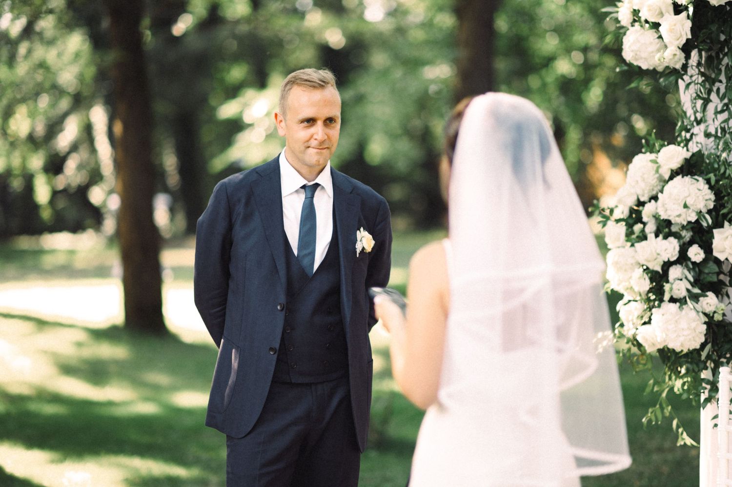 Outdoor wedding ceremony with floral arch and natural greenery backdrop.