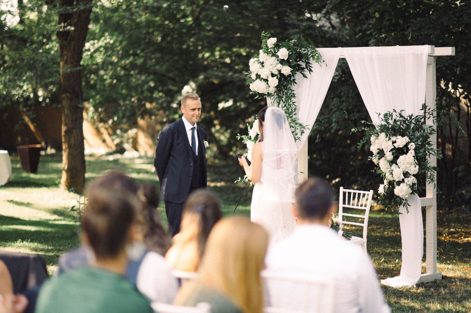 Garden wedding ceremony setup with white fabric arch and floral decorations.