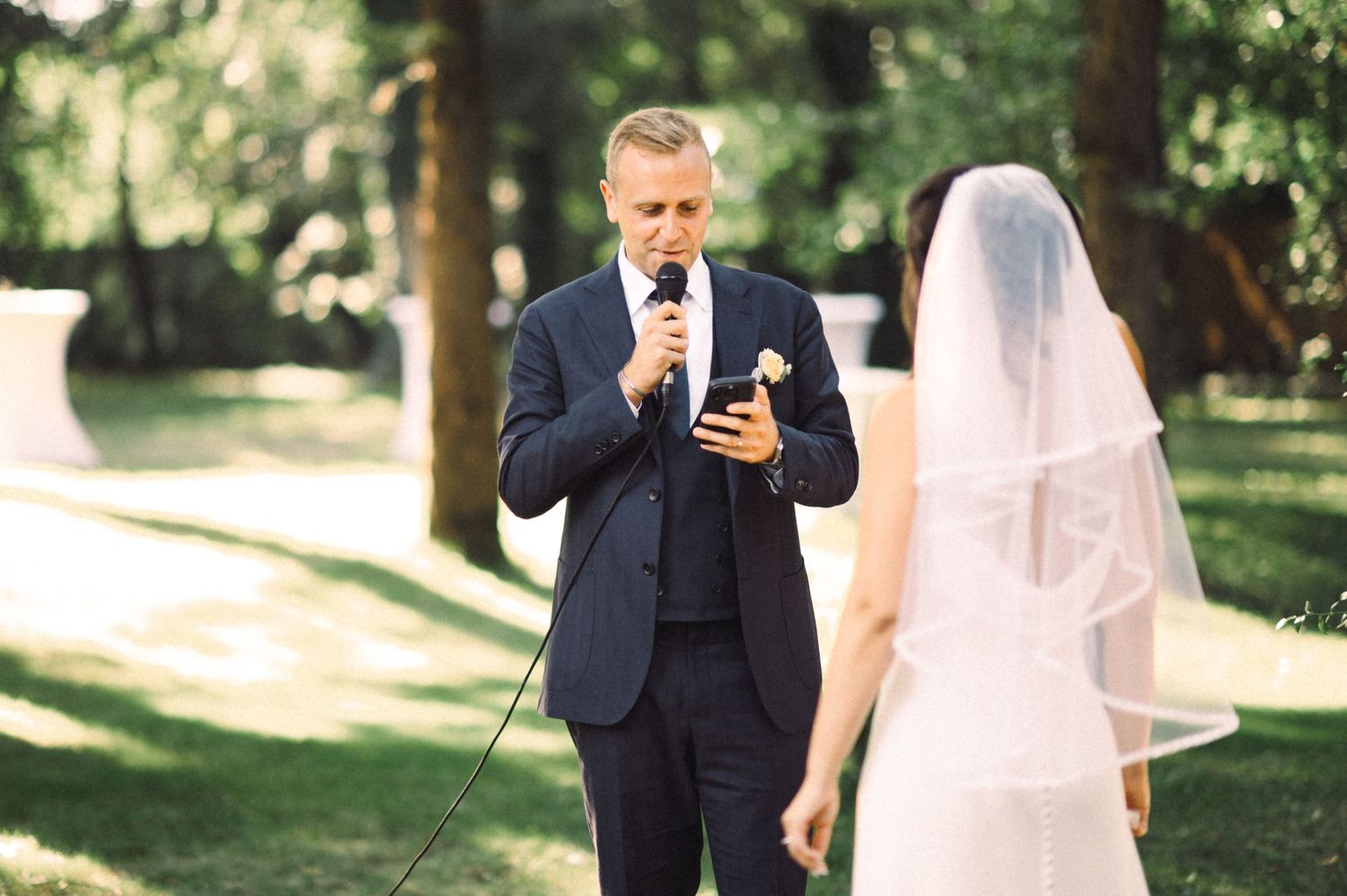 Outdoor wedding ceremony with white floral arch in a natural garden setting.