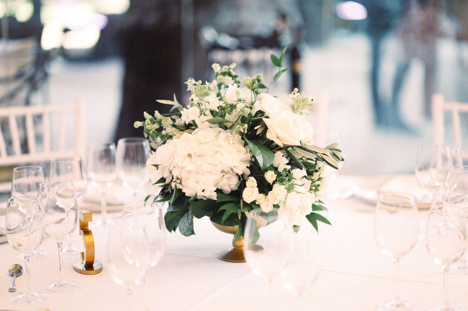 An elegant white floral centerpiece with greenery on a formal dining table setting.