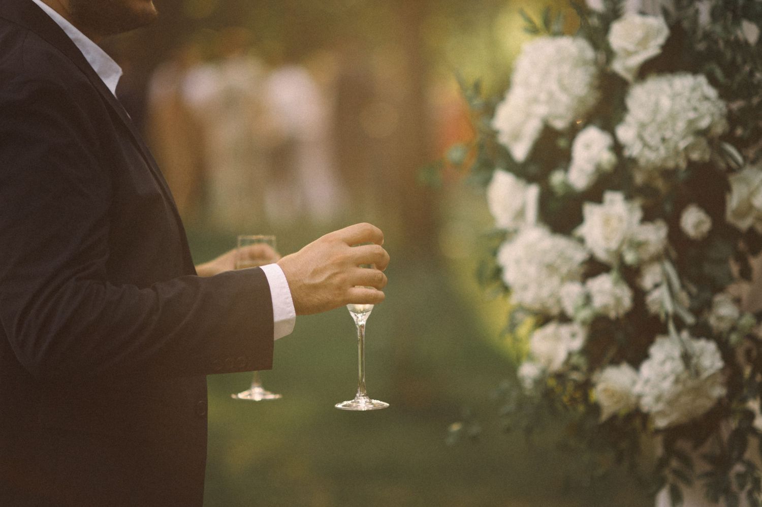 Close-up of hands holding champagne glasses at an elegant outdoor wedding reception.