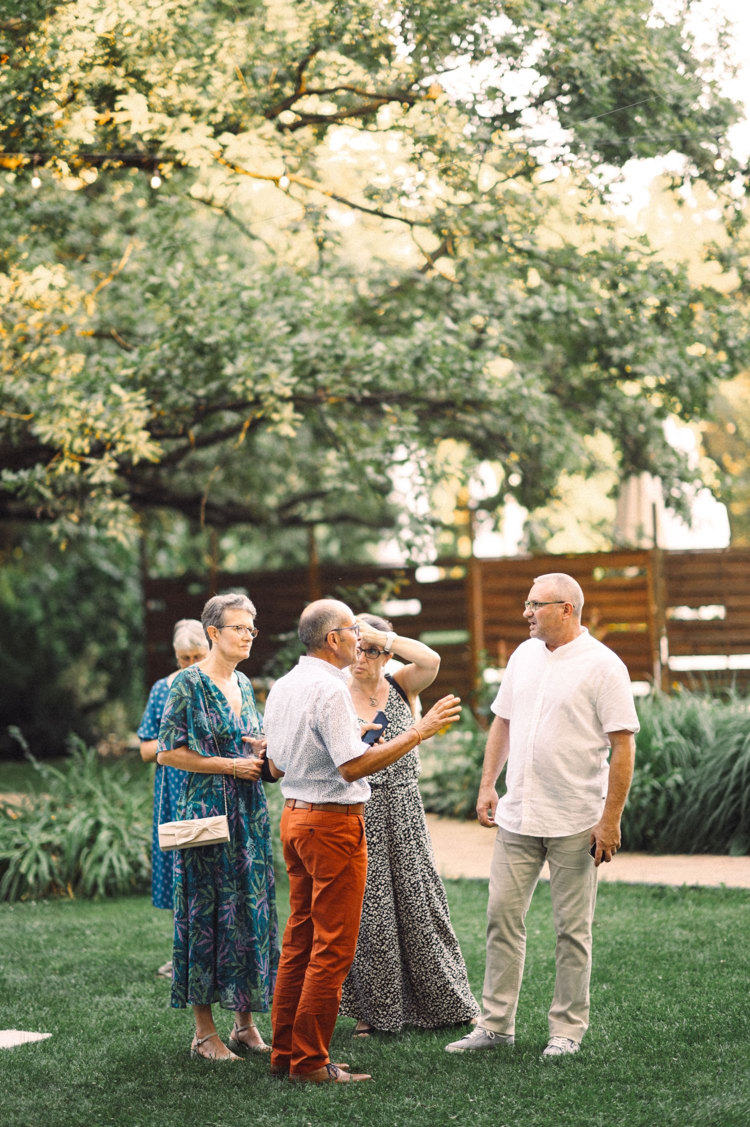 A small group engaged in casual conversation on a lush green lawn at an outdoor gathering.