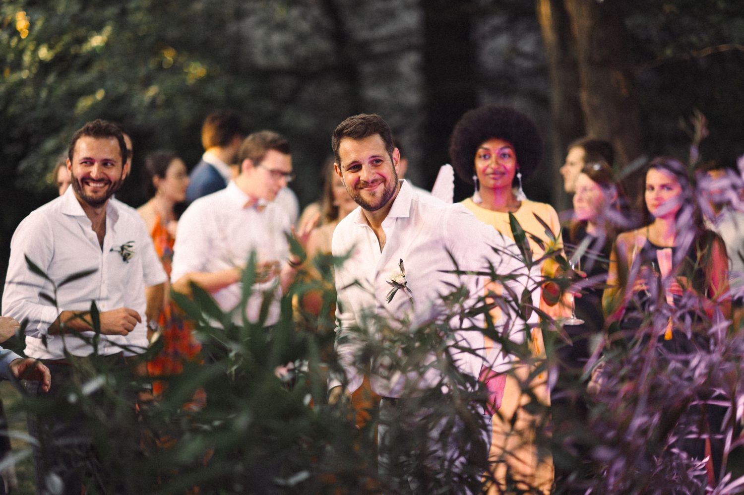 Guests enjoying a festive outdoor celebration with glowing lights and foliage.