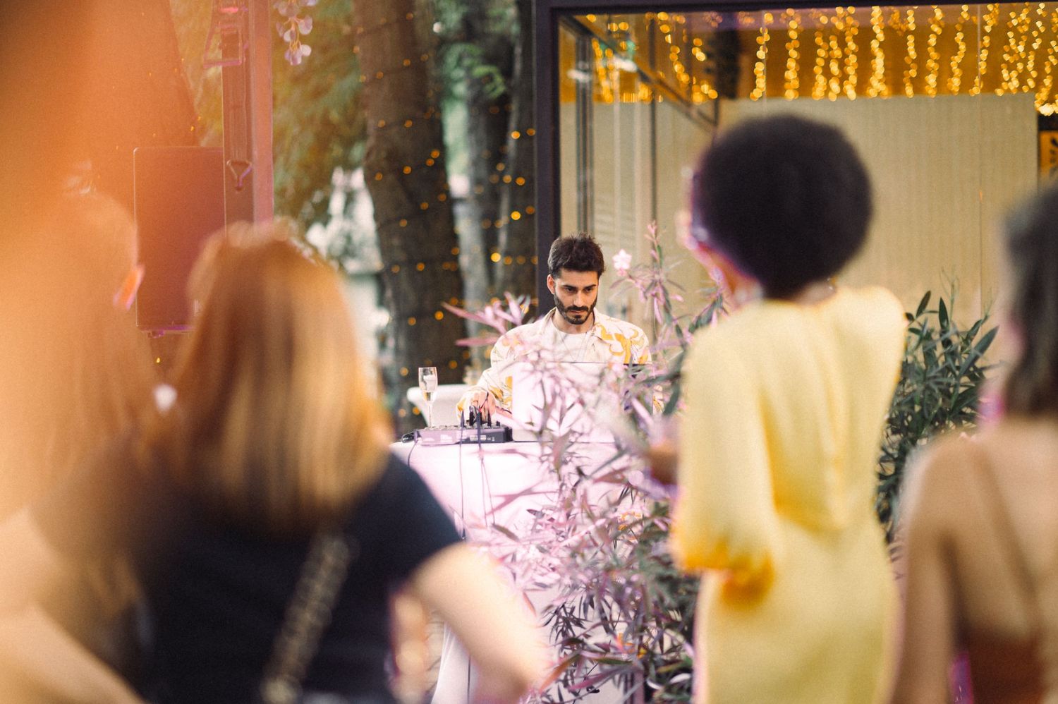 Party guests mingling at an outdoor celebration with string lights and floral decorations.