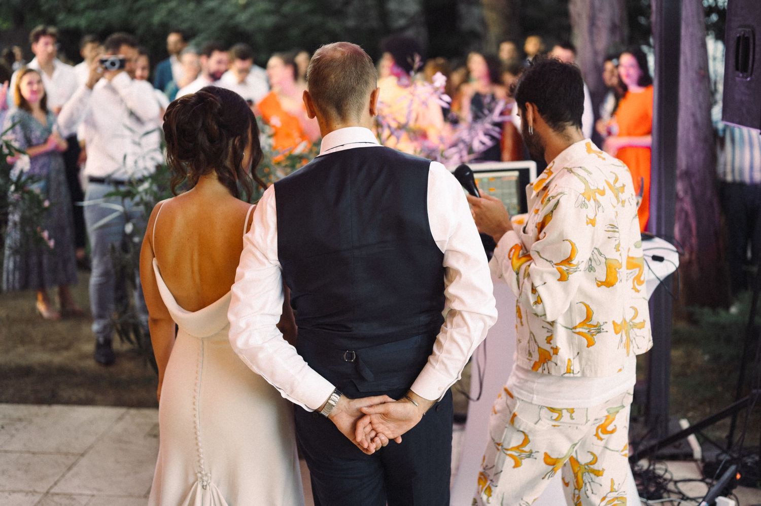 Wedding guests standing together at an outdoor reception with decorative lighting.