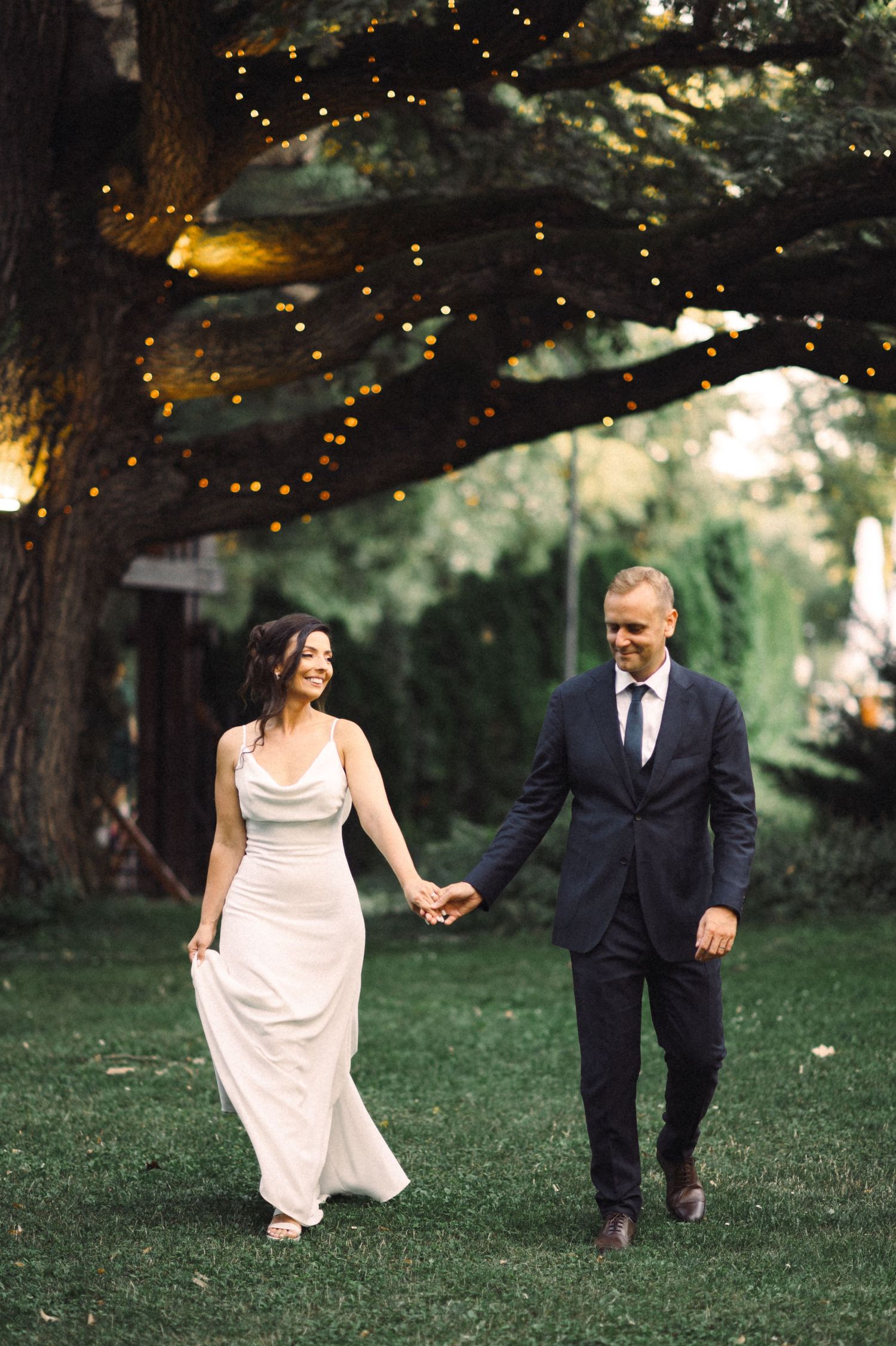 Romantic evening wedding photo under a tree decorated with twinkling fairy lights.
