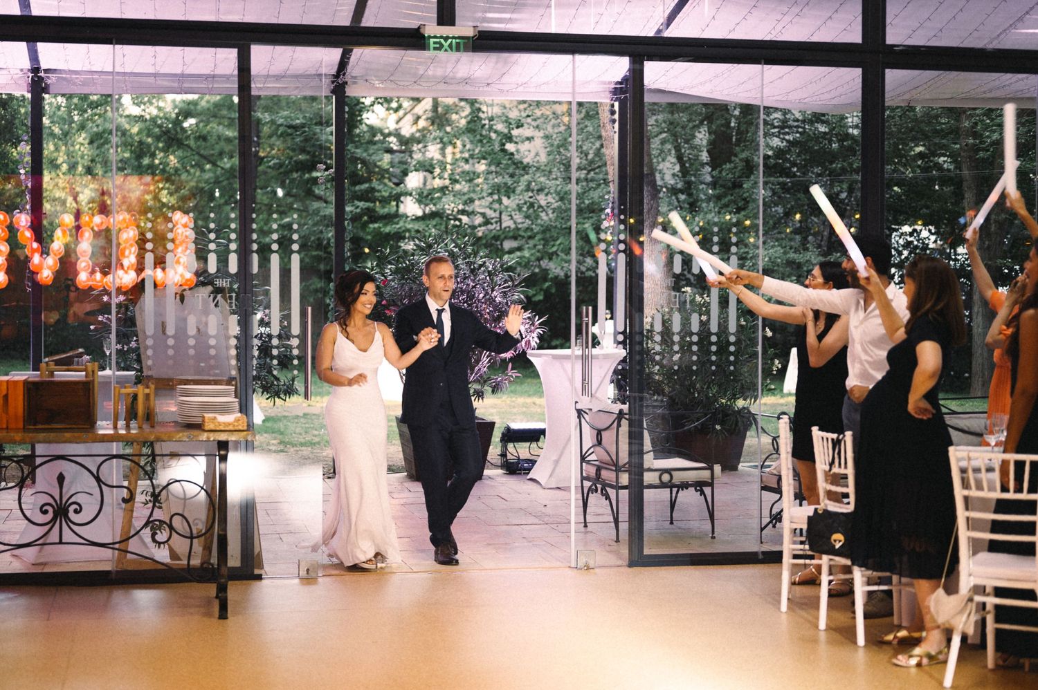 Wedding reception dance party with guests holding light-up wands in a covered outdoor venue.