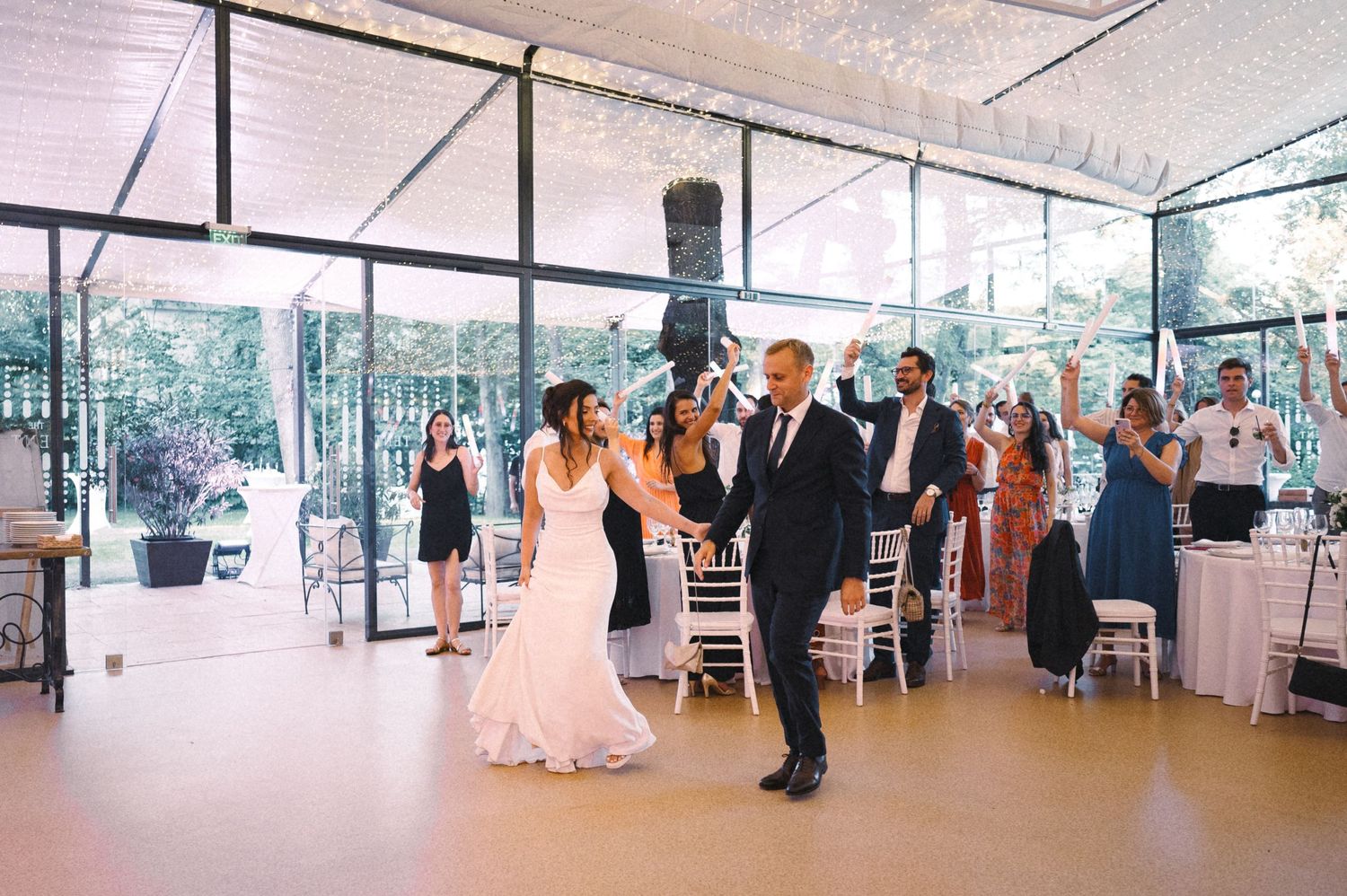 First dance at an elegant glass-enclosed wedding reception venue surrounded by guests.
