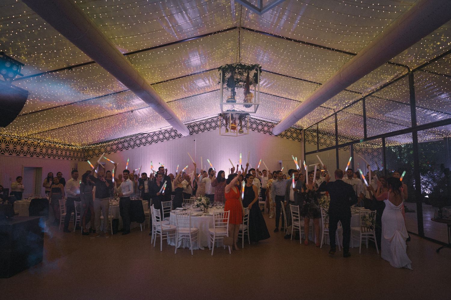 Dimly lit wedding reception venue with guests dancing under twinkling lights and decorative ceiling.