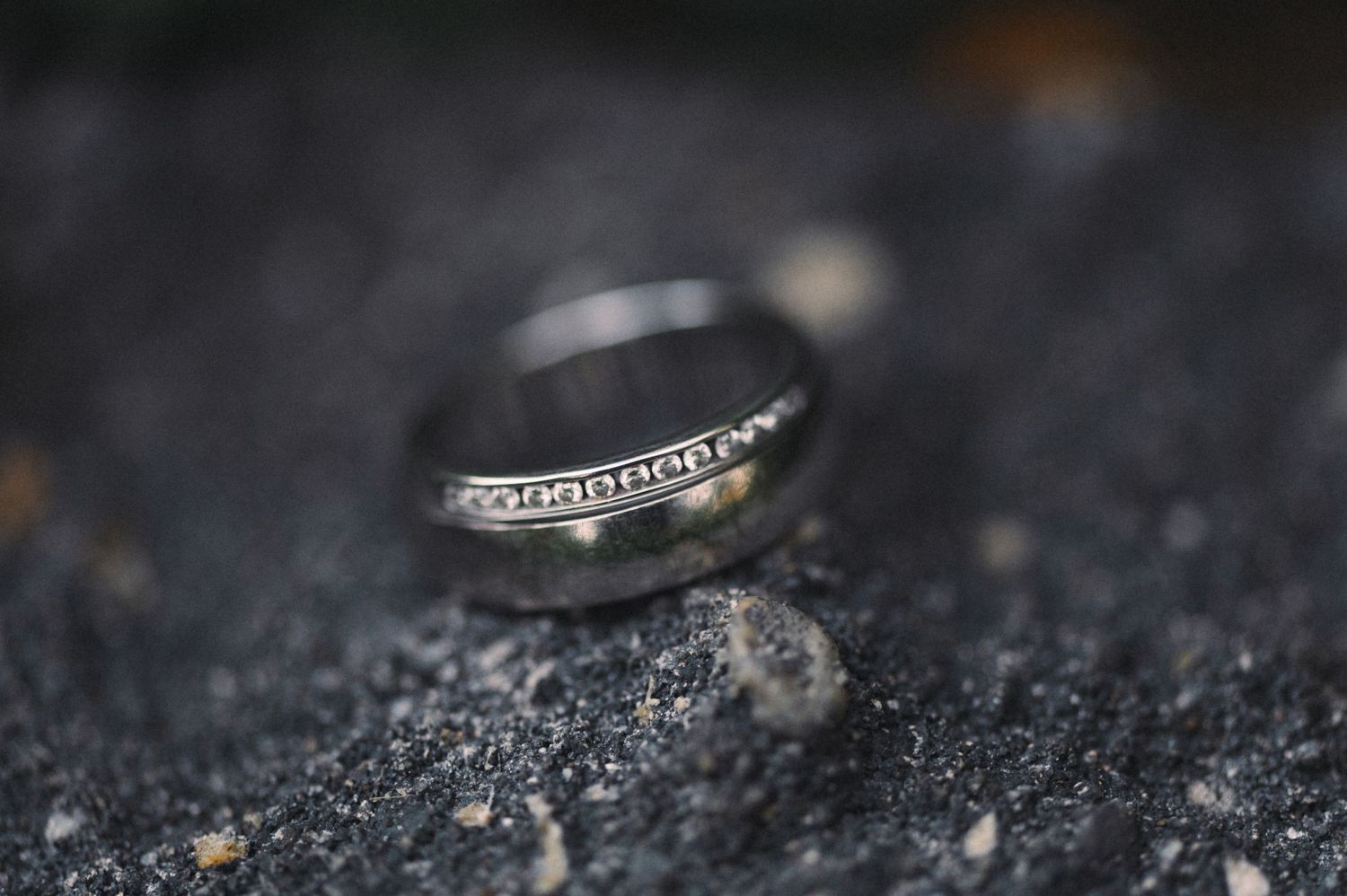 Macro shot of a diamond wedding ring on dark textured surface.