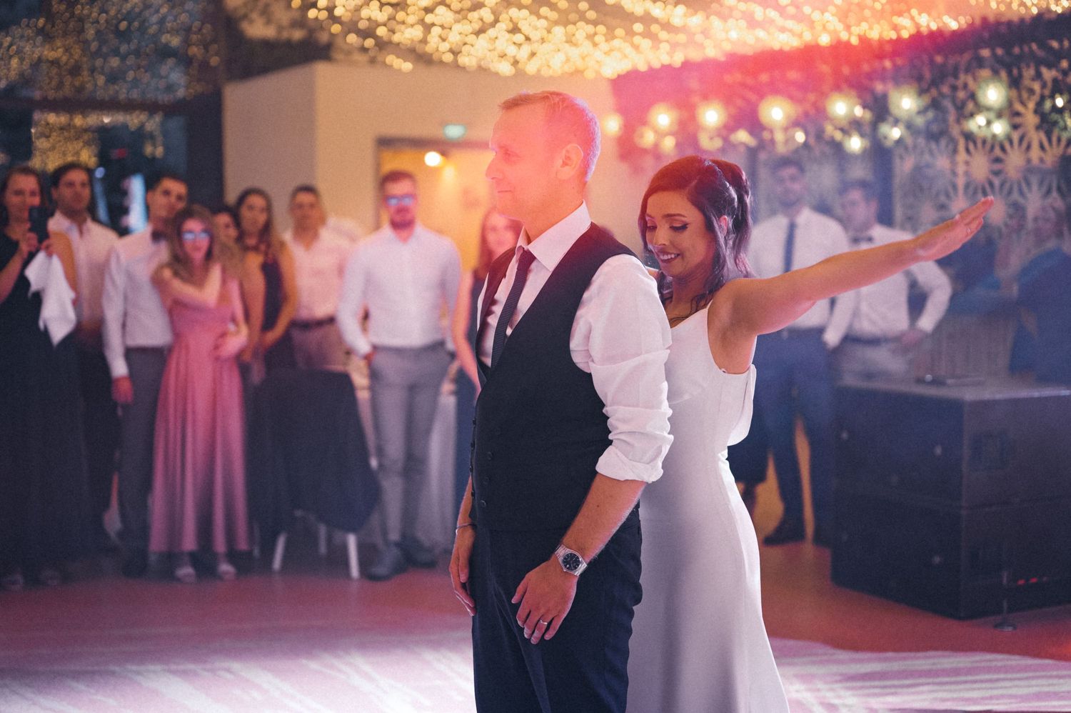 First dance at wedding reception under pink mood lighting and string lights.