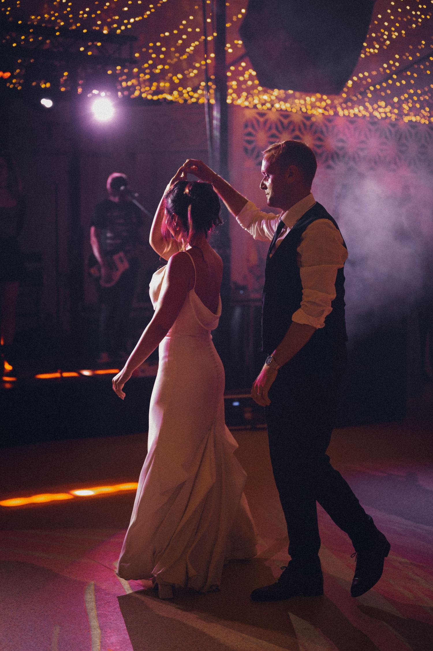 A couple dancing under twinkling lights and pink smoke at their wedding reception.