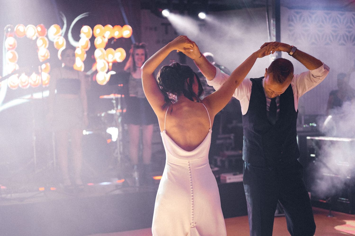 Dancing couple in formal attire twirling under atmospheric lighting at a wedding reception.