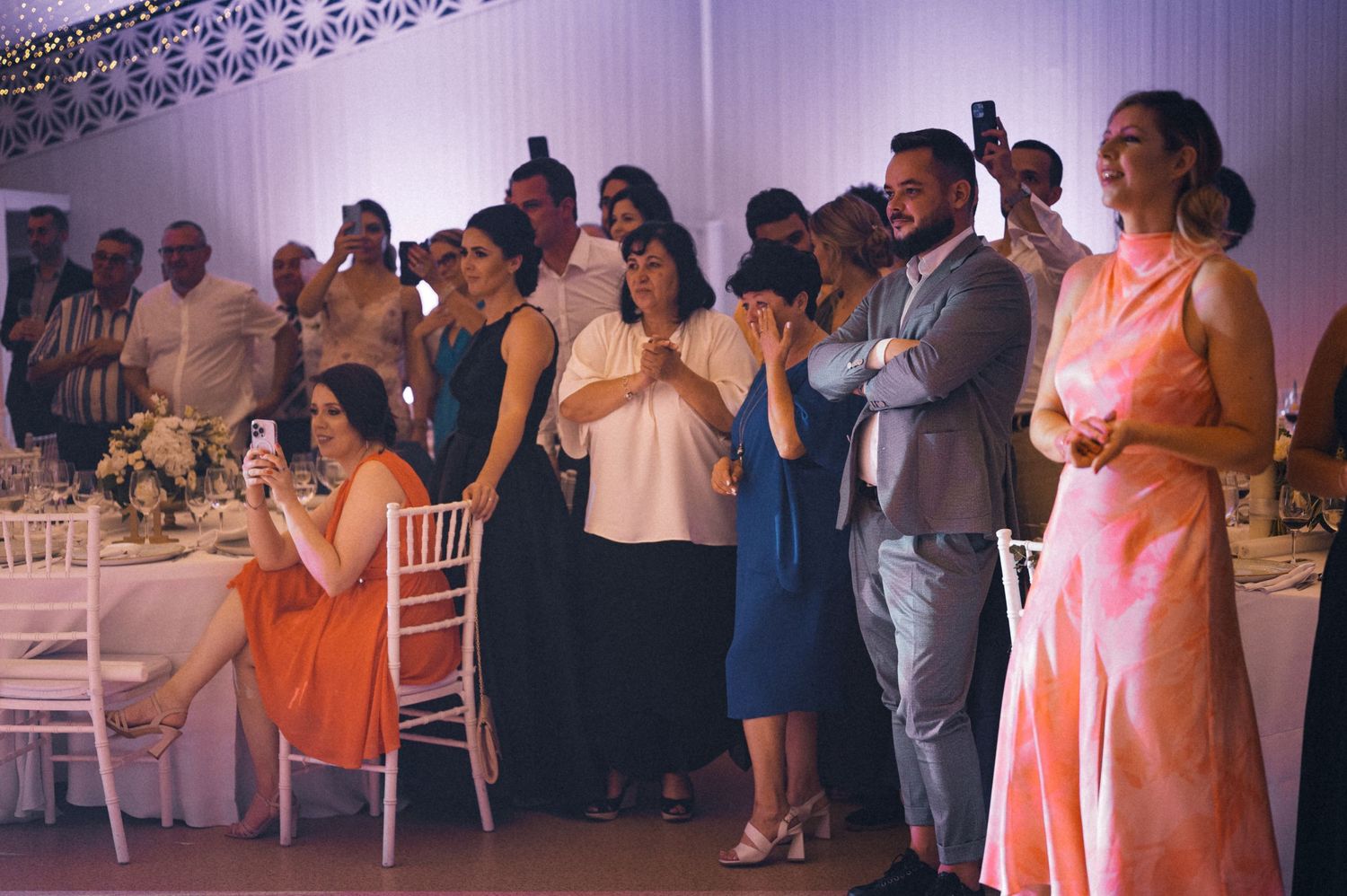 Wedding guests in colorful attire watching the celebration from their reception tables.