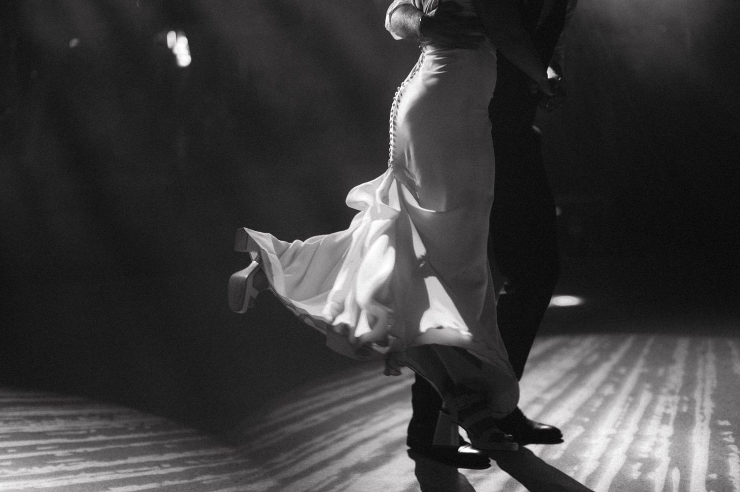A black and white capture of a dancing couple's flowing dress movement on the dance floor.