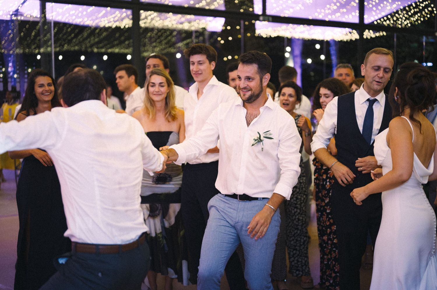 Guests mingling and dancing at an evening reception with purple mood lighting.