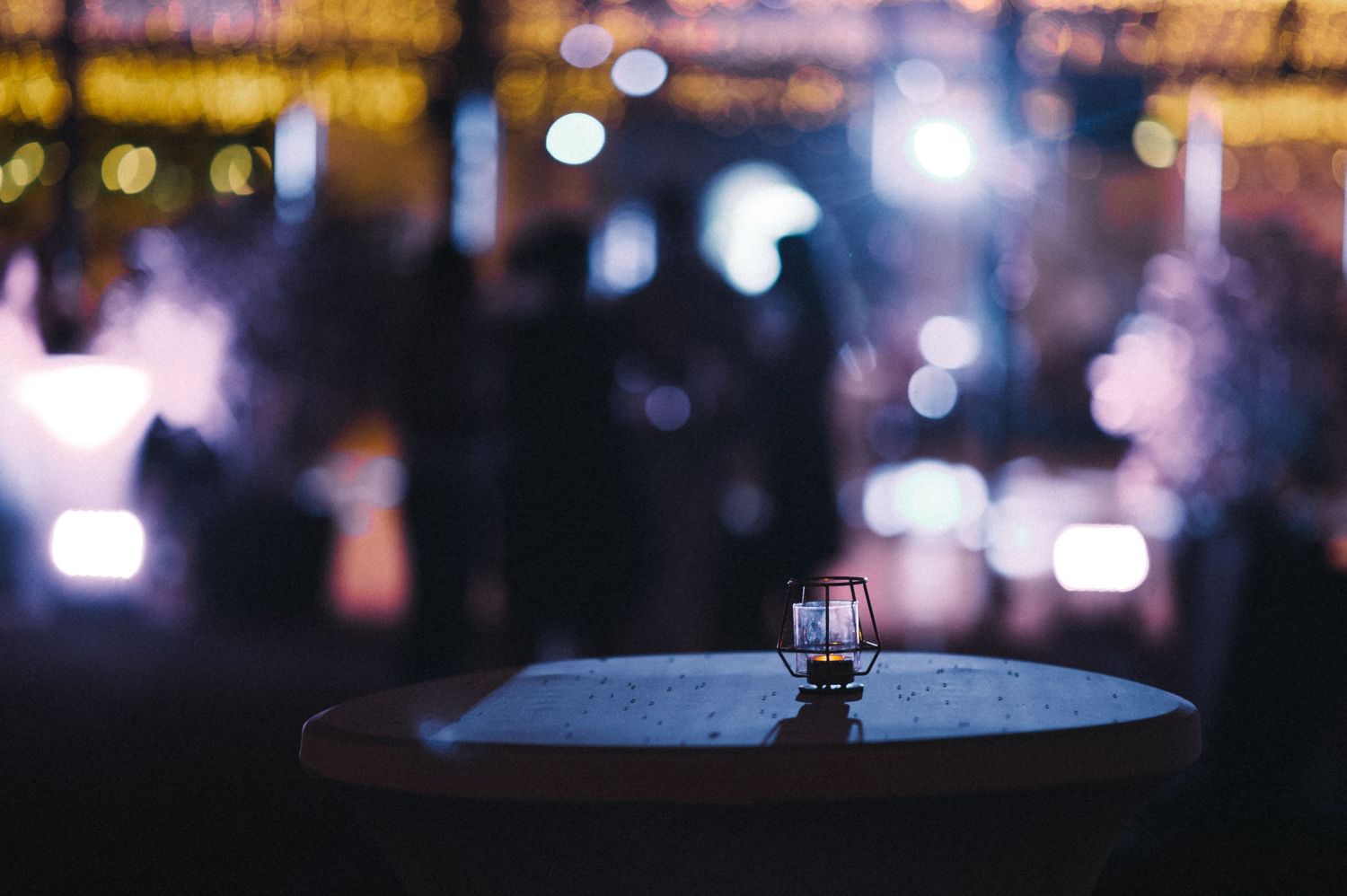 A single glass sits on a table with blurred bokeh lights in the dark background.