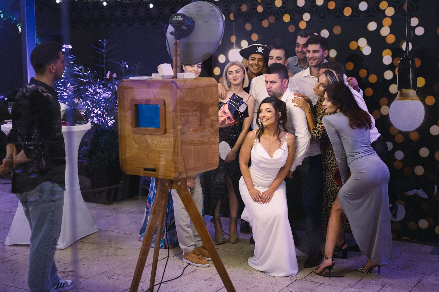 Wedding guests gathered around a vintage camera at an evening reception.
