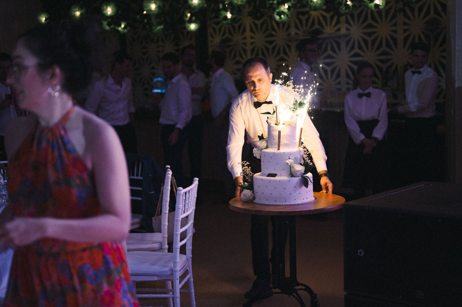 Server presenting a lit wedding cake in a dimly lit reception venue.