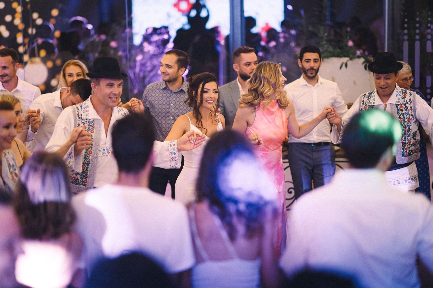 Wedding reception guests dancing and celebrating under decorative lighting.
