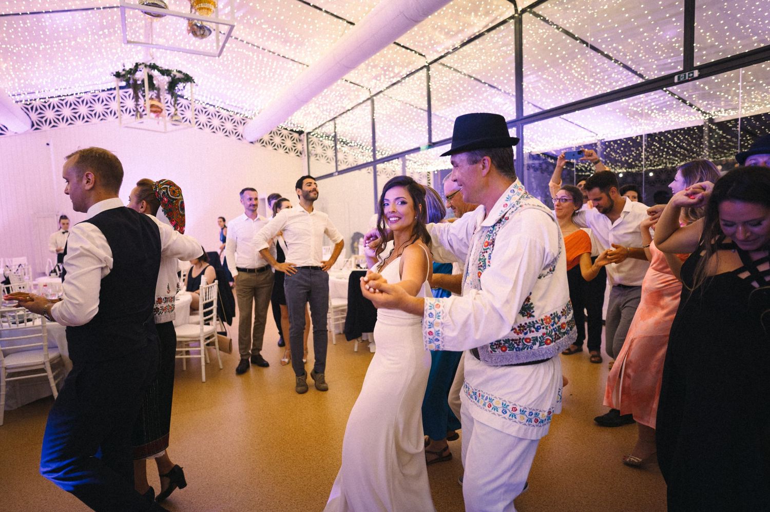 Couples dancing at a wedding reception in an indoor venue with string lights overhead.