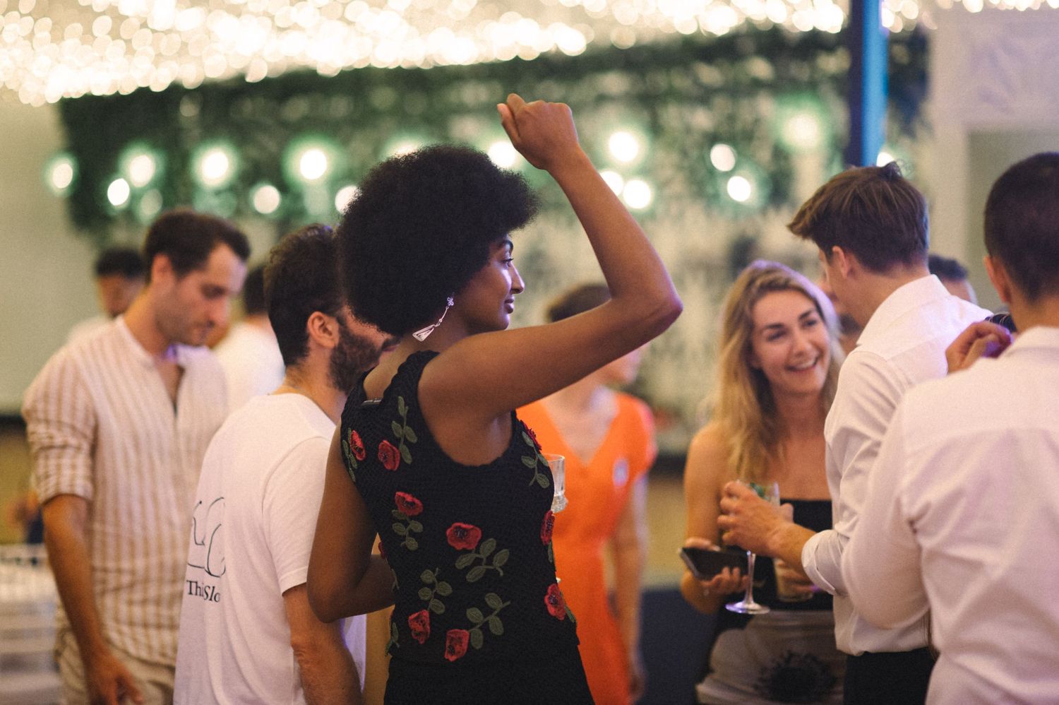 Party guests dance and socialize under decorative greenery and string lights at reception.