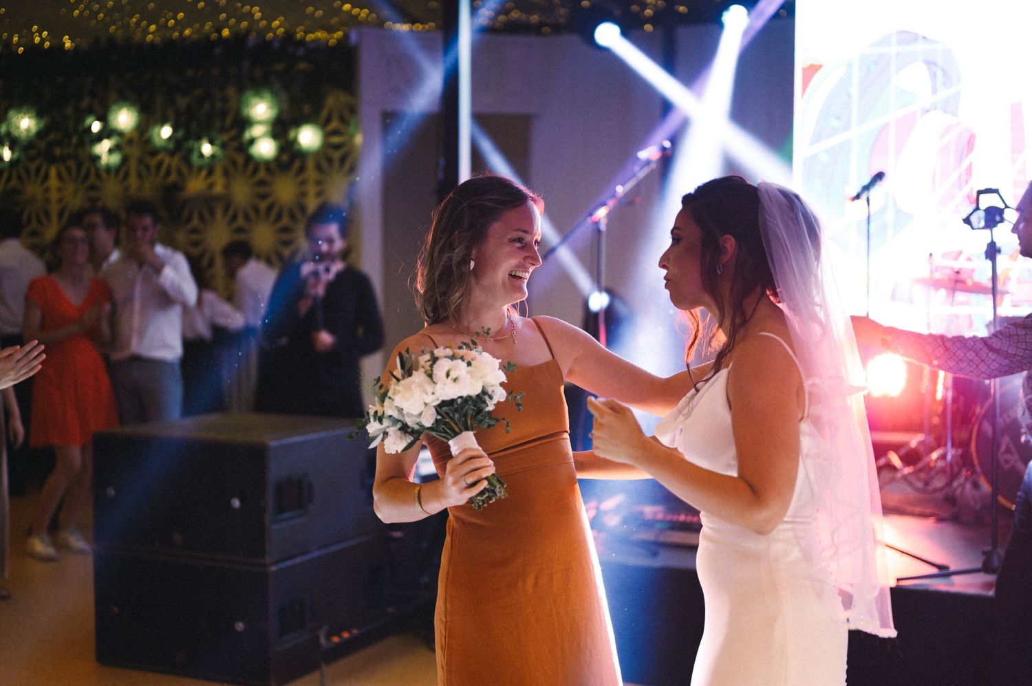 Two people sharing an emotional moment on a dance floor while holding bouquets at a wedding reception.