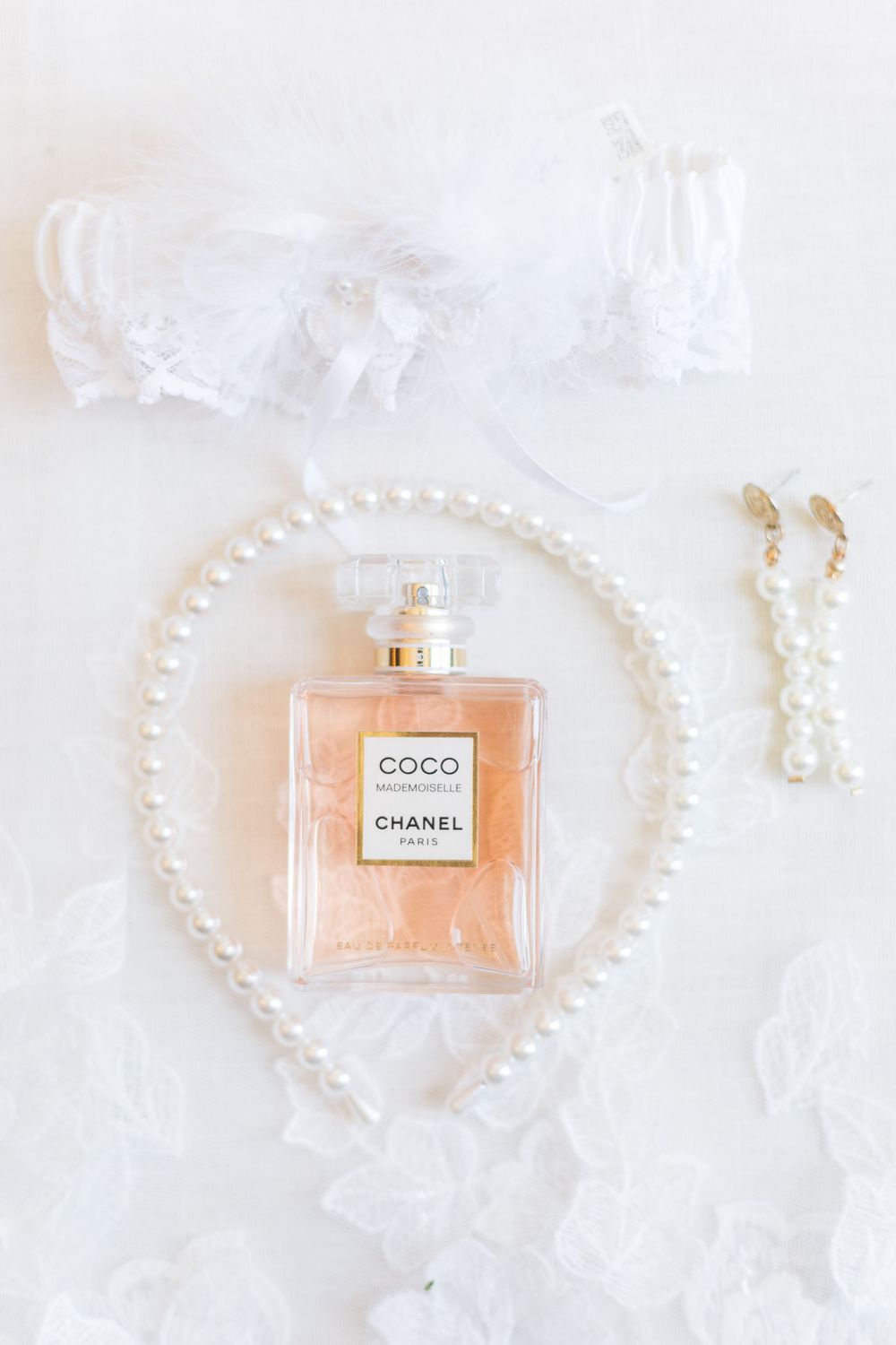 Chanel Coco perfume bottle surrounded by pearls and white tulle on a light background.