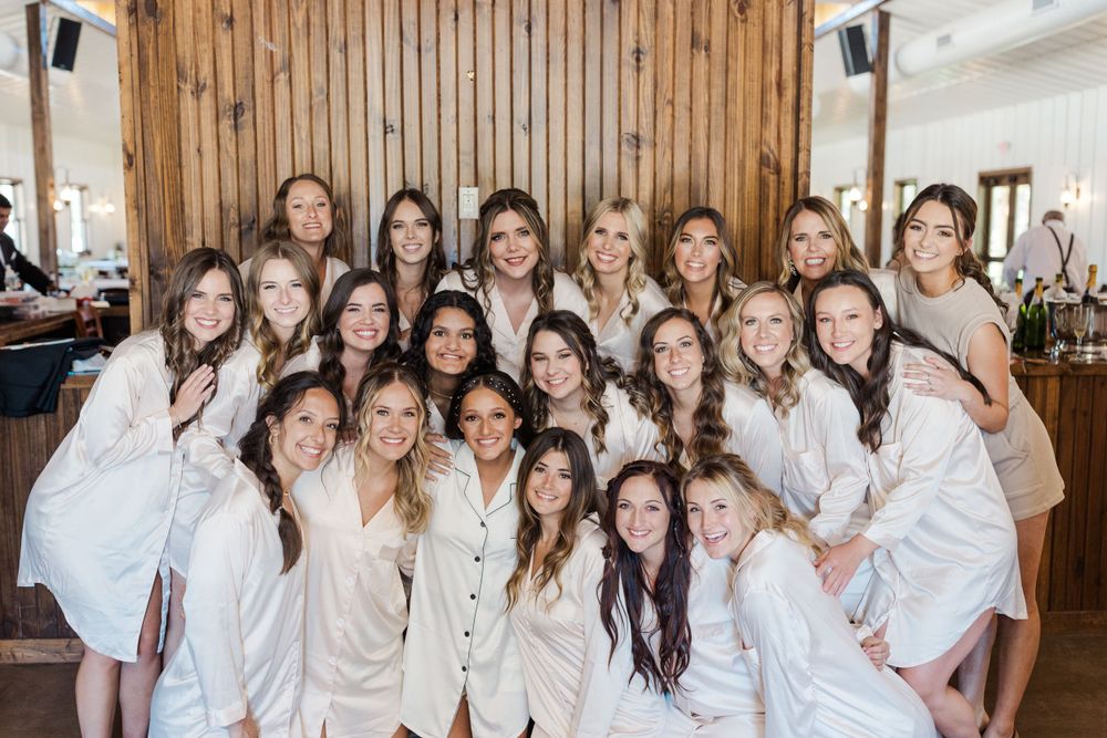 Large group wearing matching cream-colored robes poses together in a rustic wood-paneled room.