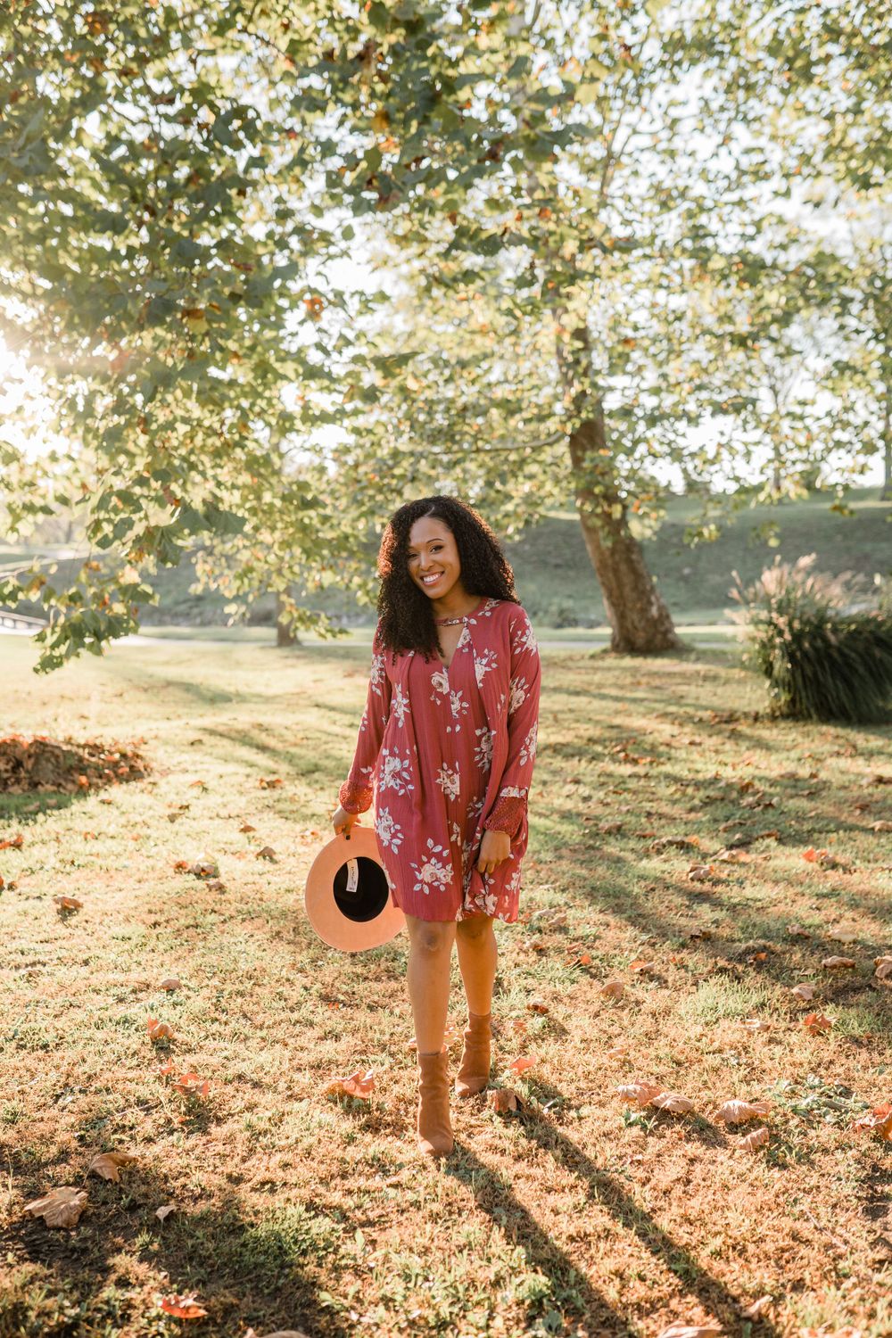 Person in red floral dress walking through sun-dappled autumn garden.