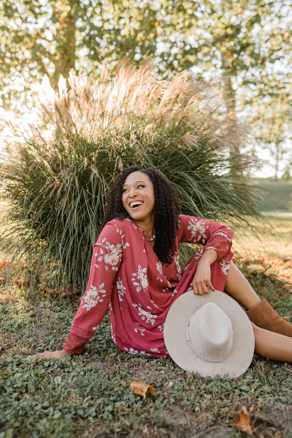 Person in floral dress relaxing by ornamental grass with white hat.