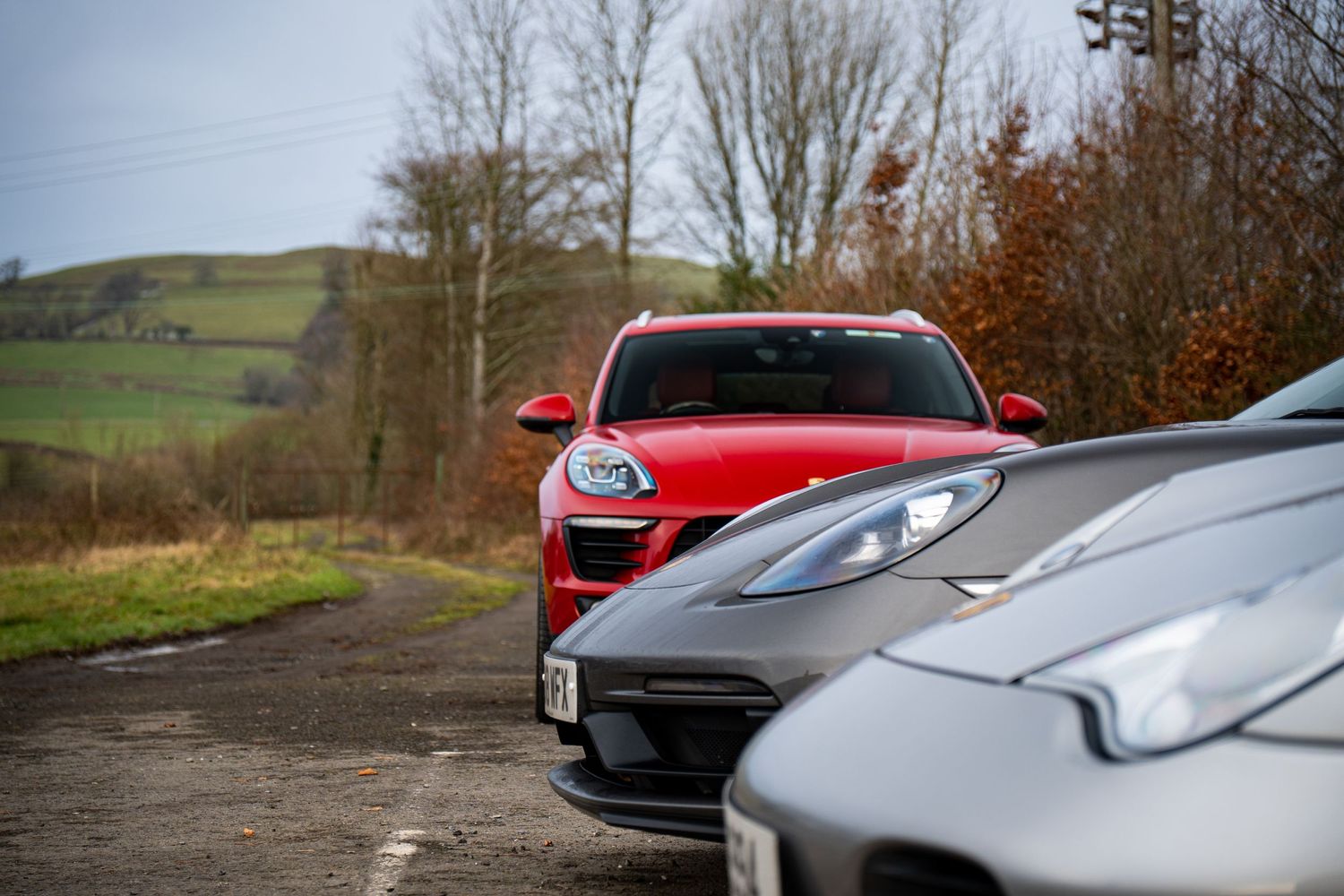 Close-up of luxury sports cars including a red Porsche lined up on a rural road.