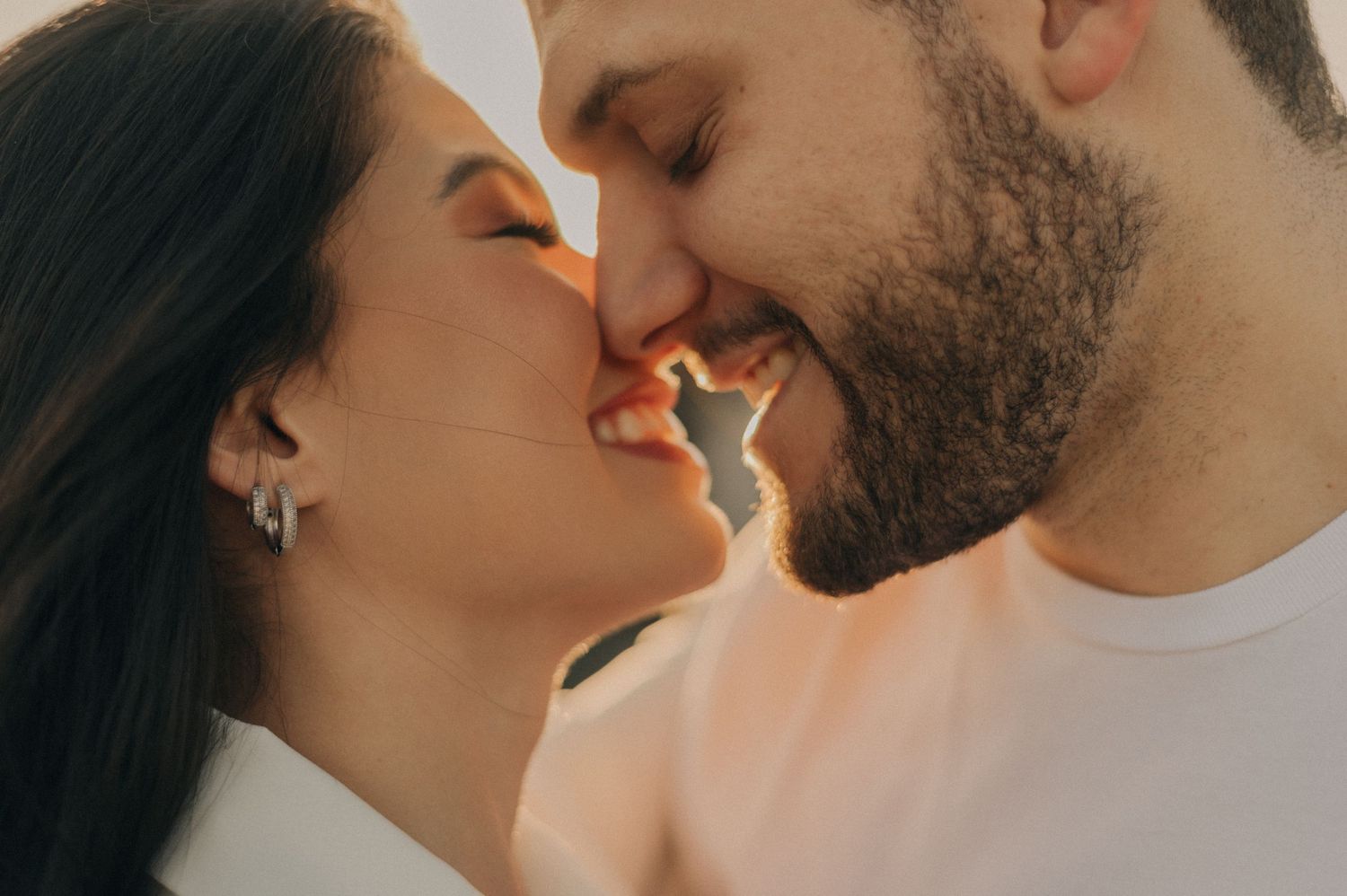 An intimate close-up portrait of a couple sharing a tender almost-kiss in warm sunlight.