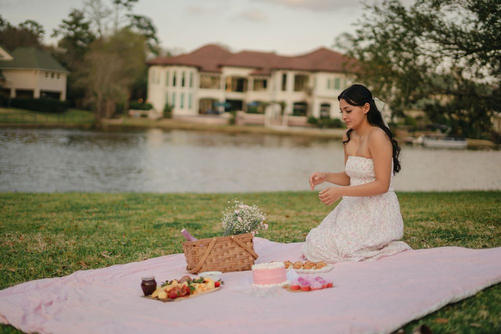 A romantic lakeside picnic setup with a white blanket, wicker basket and elegant spread by the water.