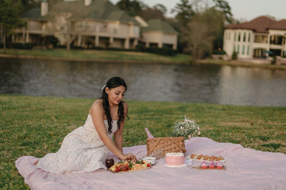 Elegant picnic setup with white lace dress and wicker basket by a scenic lake.