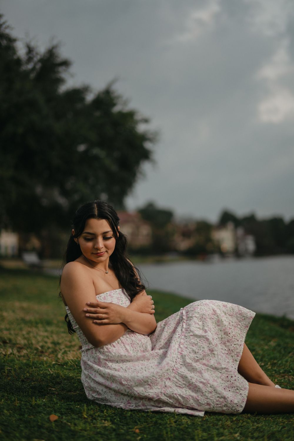 Dreamy outdoor portrait session on grass by a lake with moody storm clouds.