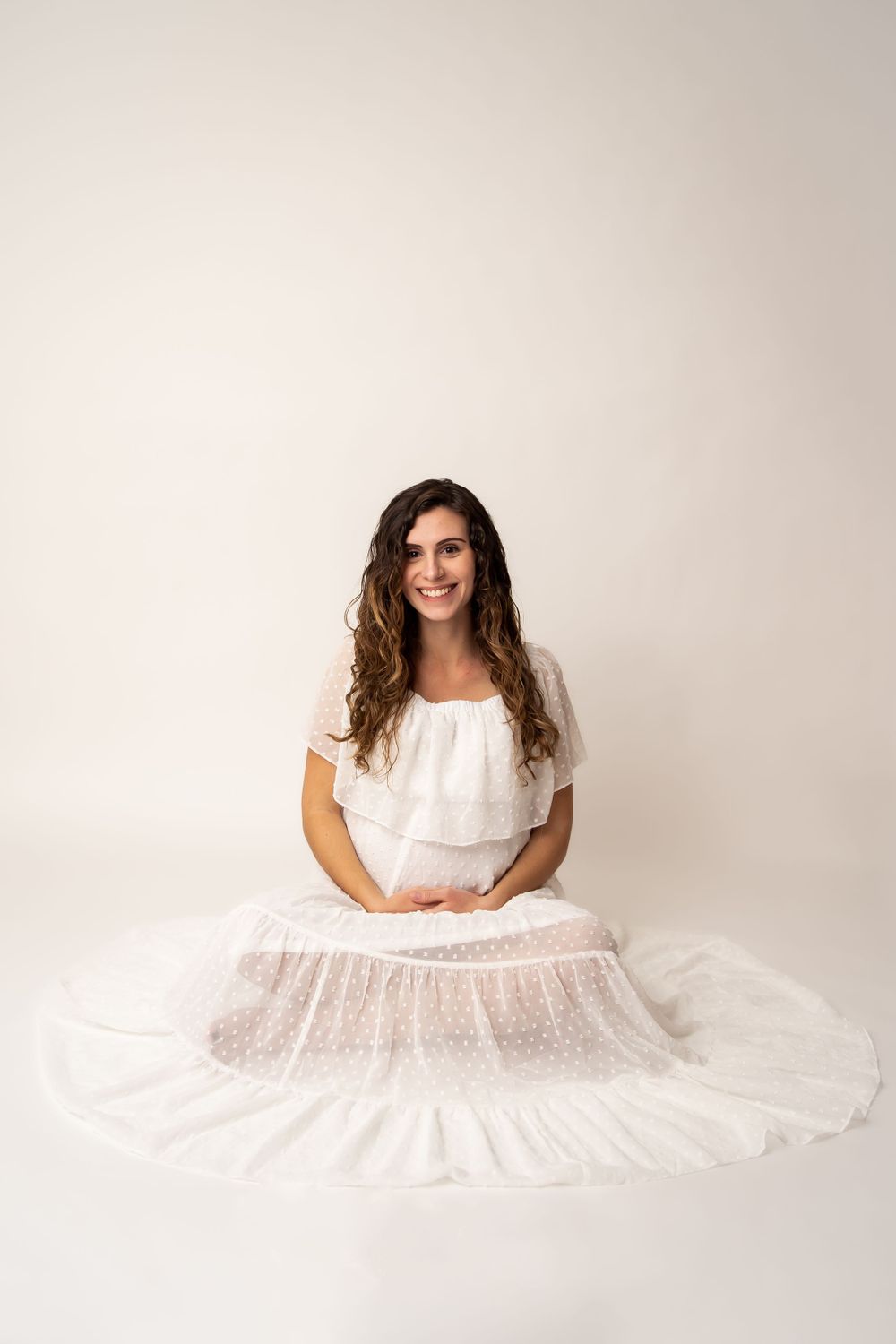 A portrait of someone wearing a flowing white dress against a neutral background.