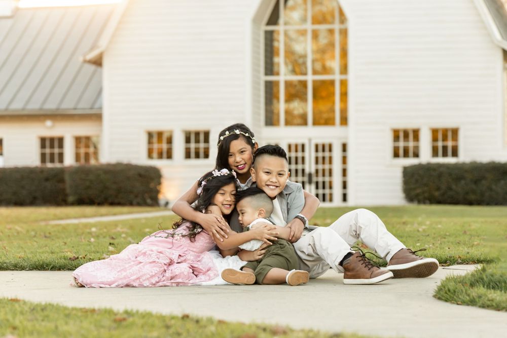 Family sitting together on grass outside a white church building on a sunny day.