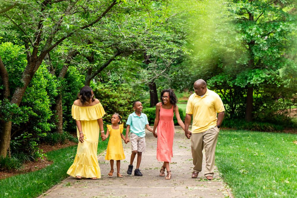 A family in coordinated yellow and coral outfits walking together on a tree-lined path.