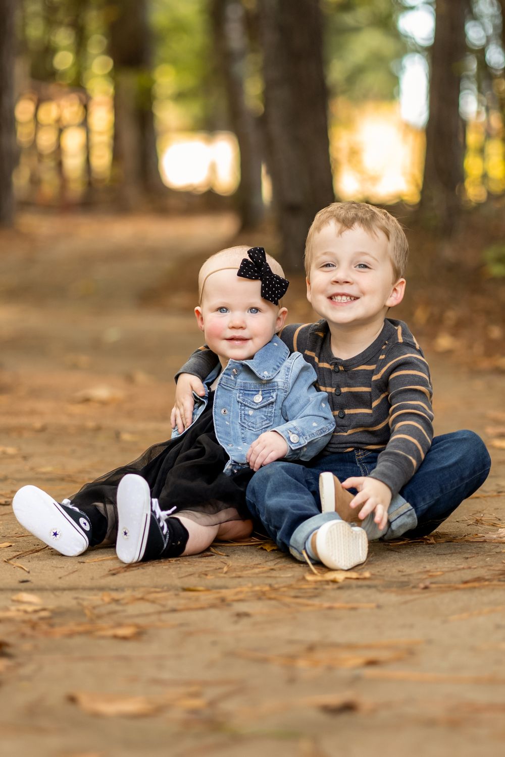 Two young children sit together on a forest path during golden hour.