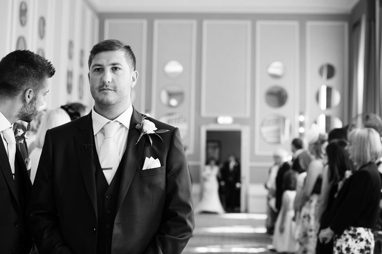 A black and white candid moment before a wedding ceremony in an elegant venue.